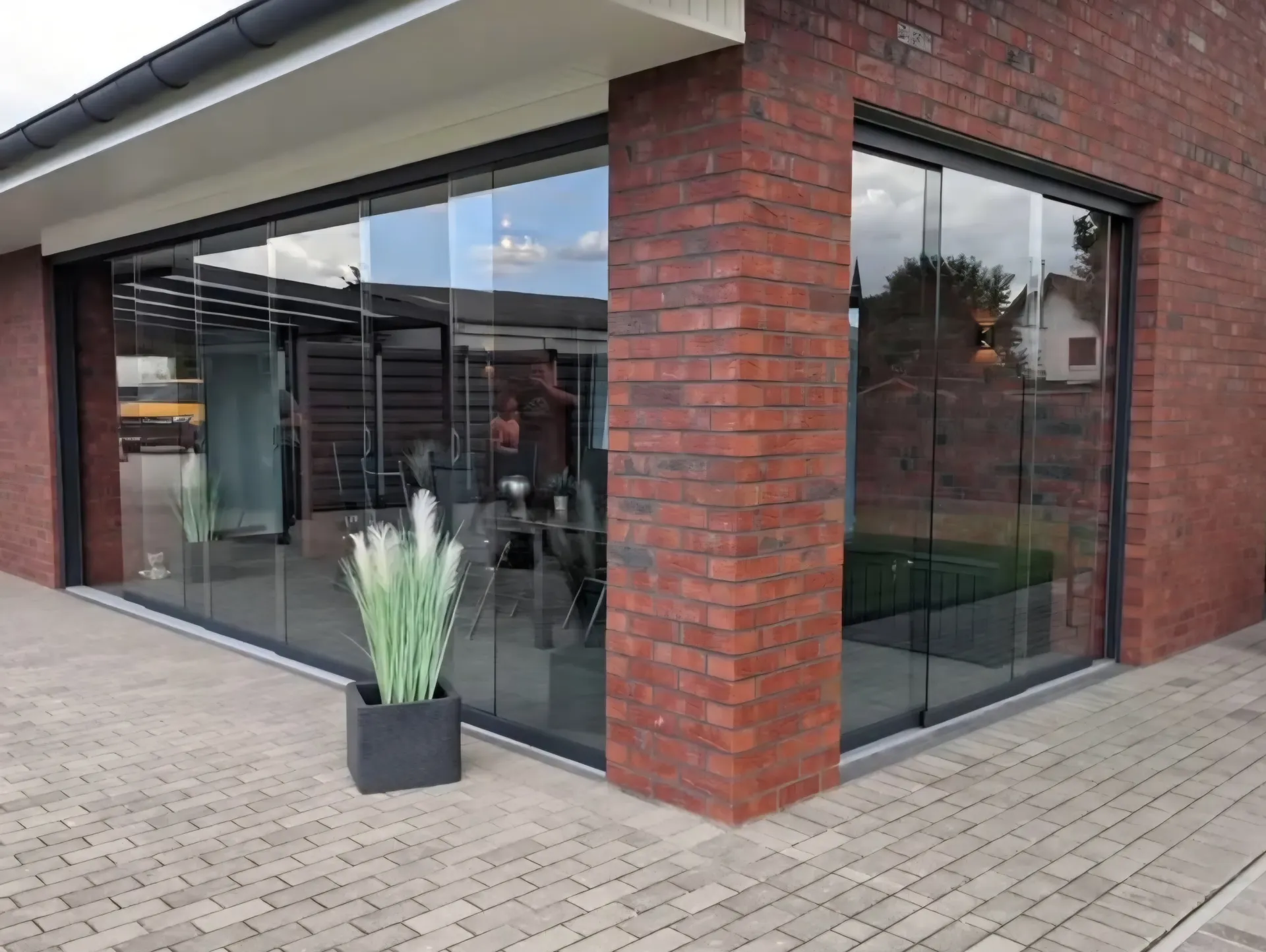 Rahmenlose Glasschiebewände um die Ecke einer Terrasse an einem Klinkerhaus